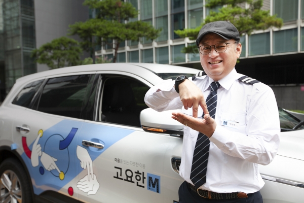 청각장애인 기사님이 수어 아티스트 '지후트리'가 '자립'이라는 수어를 이미지화해 디자인한 '고요한M' 차량 앞에서 '자립'이라는 의미의 수어를 하고 있는 모습. (사진= SK텔레콤 제공)